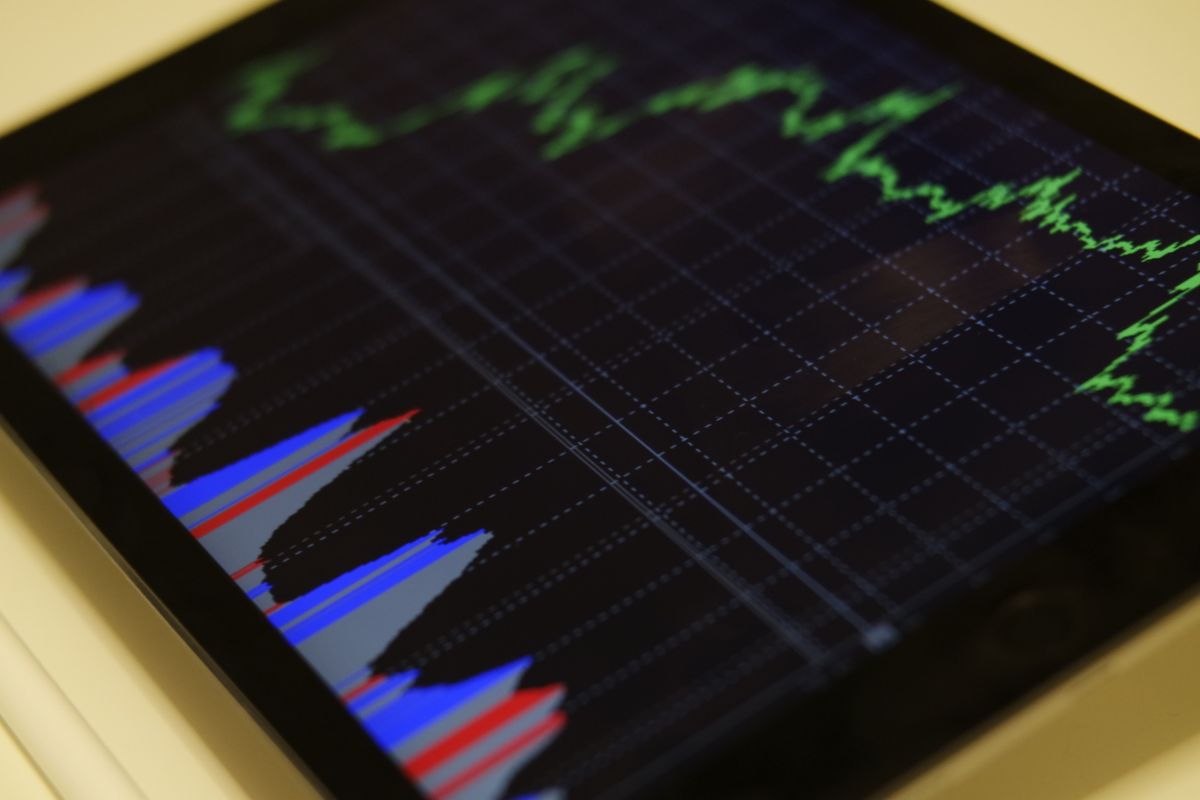 Tablet mit dunklem Finanz-Dashboard: grüne Kurslinie und farbige Indikator-Flächen unter einem feinen Punkteraster